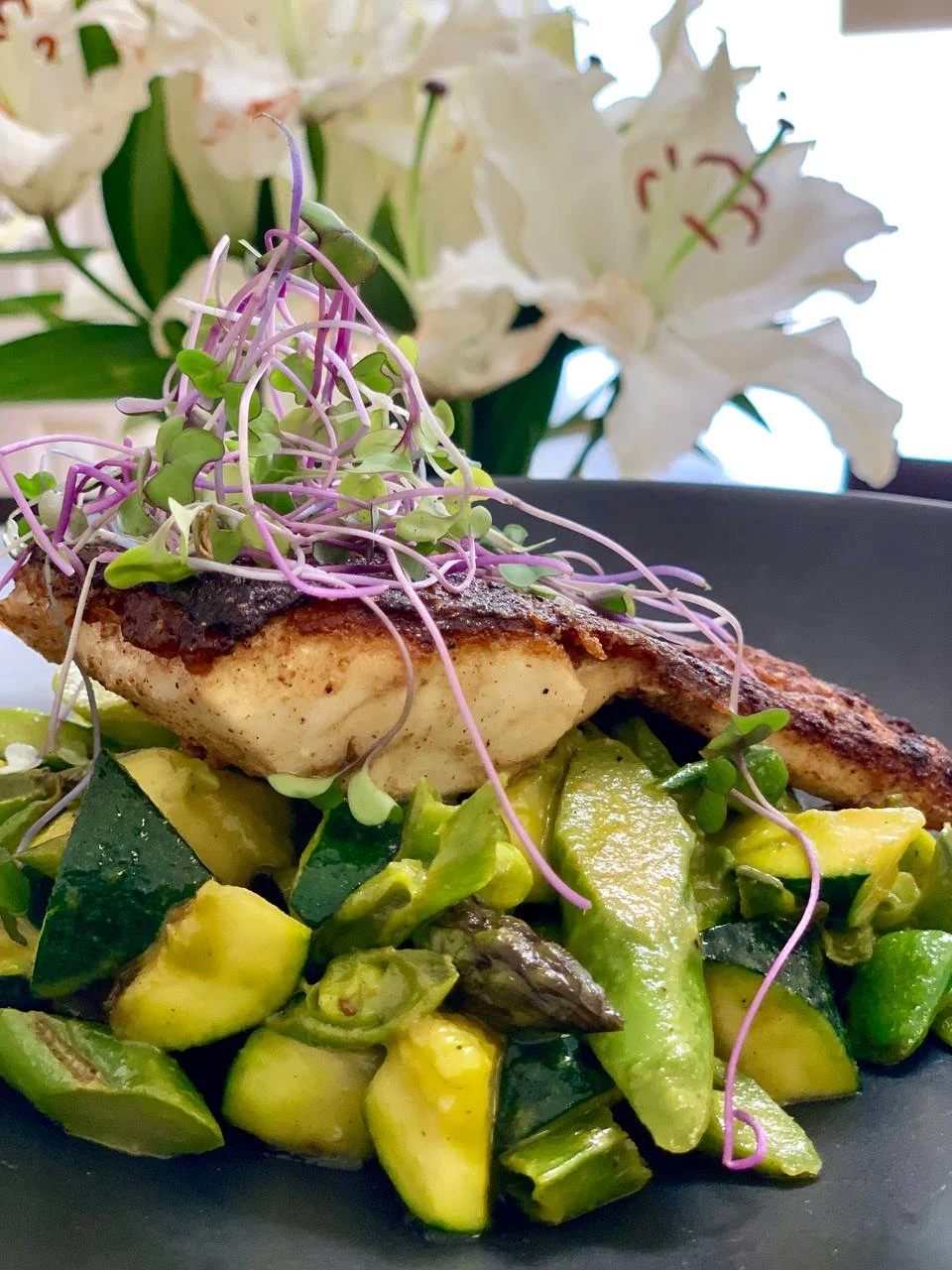 Seared fish with vegetables and microgreens on a dark plate
